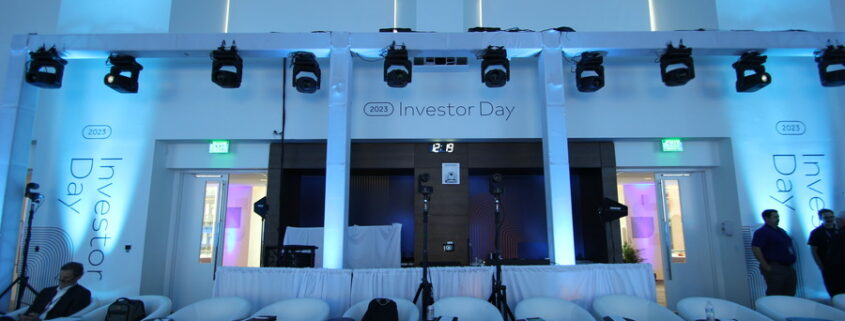 A room set up for a presentation with several white seats in rows and banners saying “2023 Investor Day.”