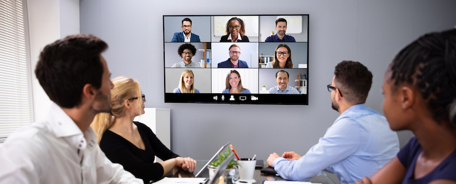 An office with four in-person employees video conferencing with remote employees. 