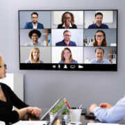 An office with four in-person employees video conferencing with remote employees.