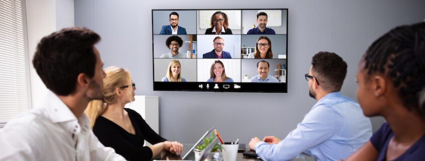 An office with four in-person employees video conferencing with remote employees.