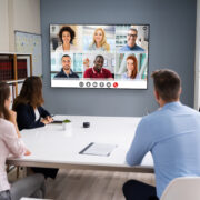 A conference room with employees gathered around a video display that shows six remote team members.