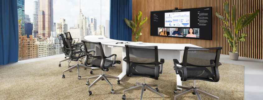 A large conference room with a semi-circle table, chairs, and video display on the board.