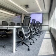 A conference room setup showing the chairs, table, and screen in the background with large windows to the right.