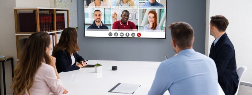 A group in a training room watching a screen with others on a conference call.